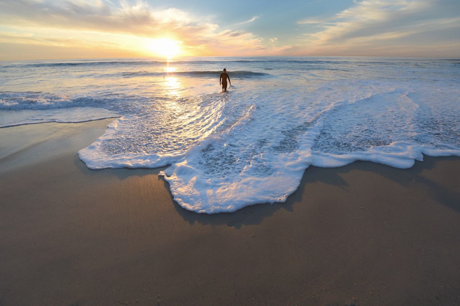 man walking on beach with sunset