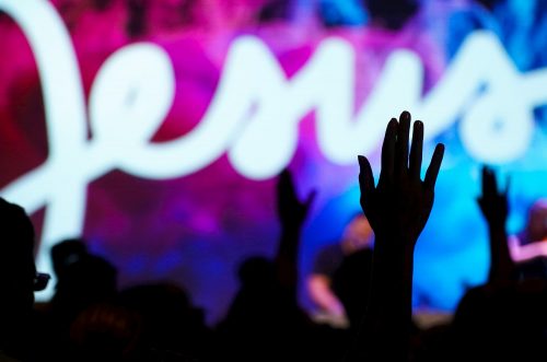 hands raised in praise in church jesus' name in background
